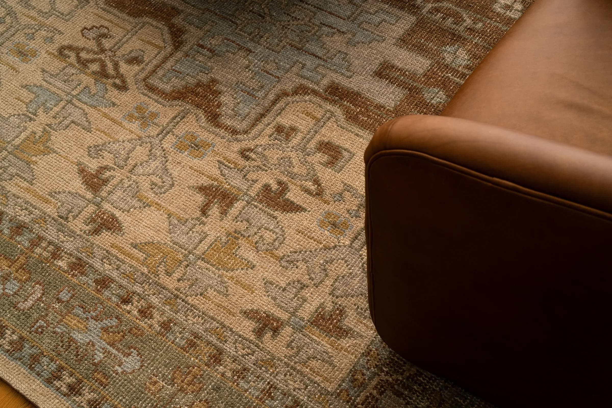 A contemporary house behind a black slatted fence with mature palms, and its interiors: a pale living room, an open kitchen and a detail of a patterned rug against leather. Frame 3 of 23.