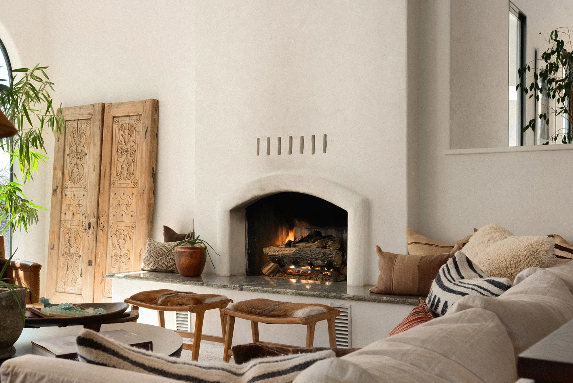 A contemporary house behind a black slatted fence with mature palms, and its interiors: a pale living room, an open kitchen and a detail of a patterned rug against leather. Frame 19 of 23.