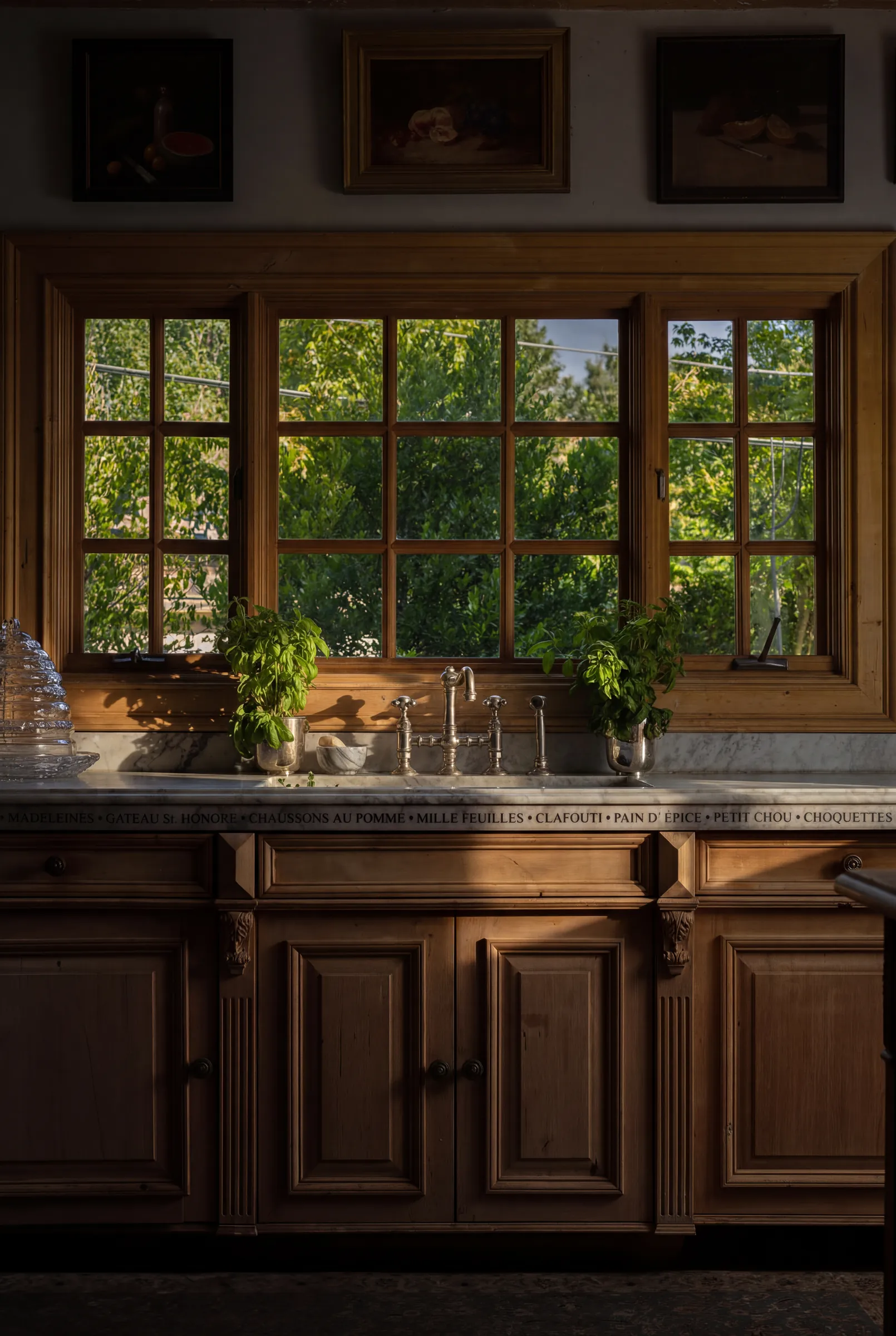 A steep-gabled house photographed at dusk with the interior lights on, its garden, leaded windows and a timber kitchen. Frame 4 of 4.